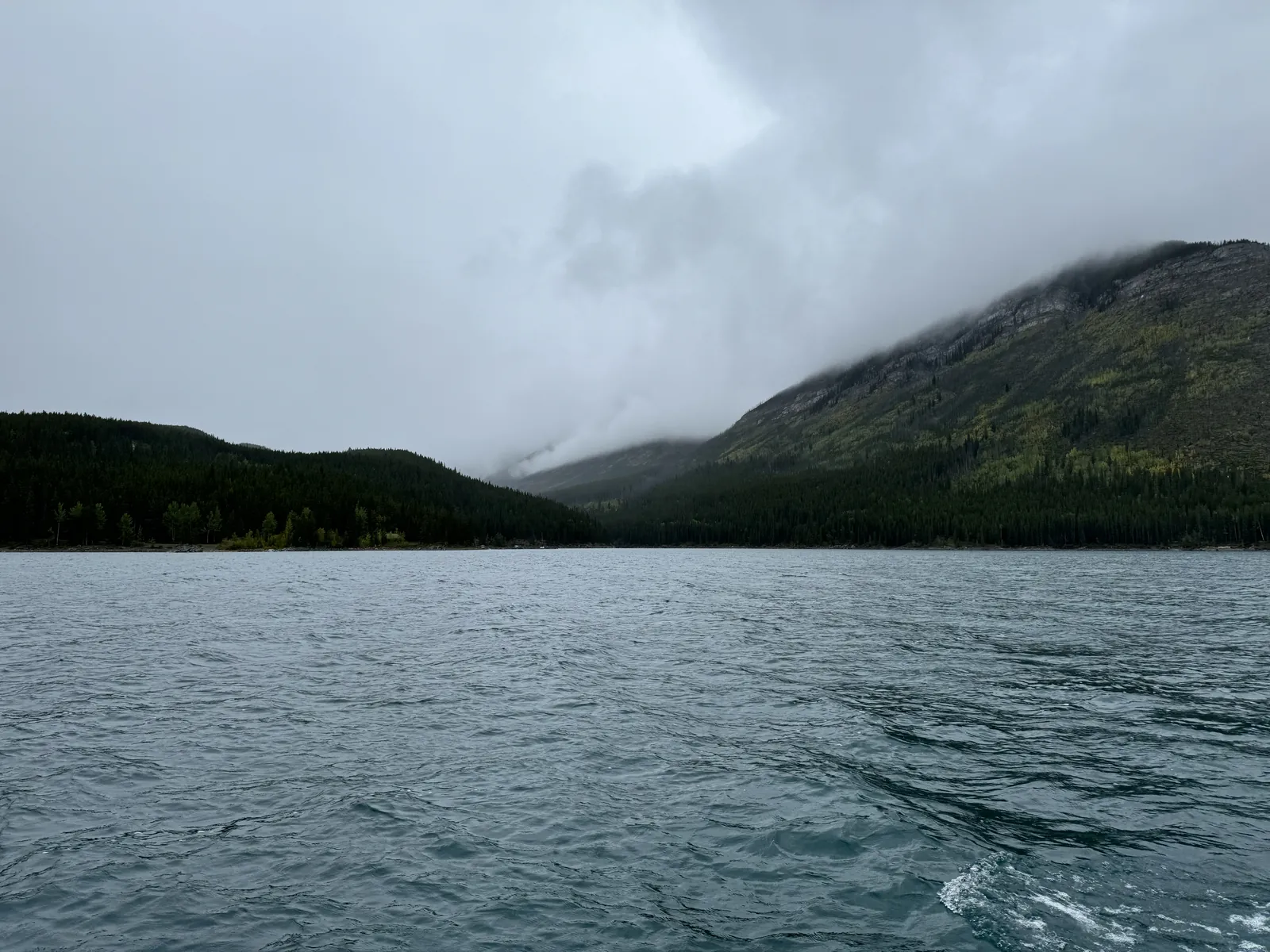 Gray-green water on Lake Minnewanka with forested mountains rising into low clouds