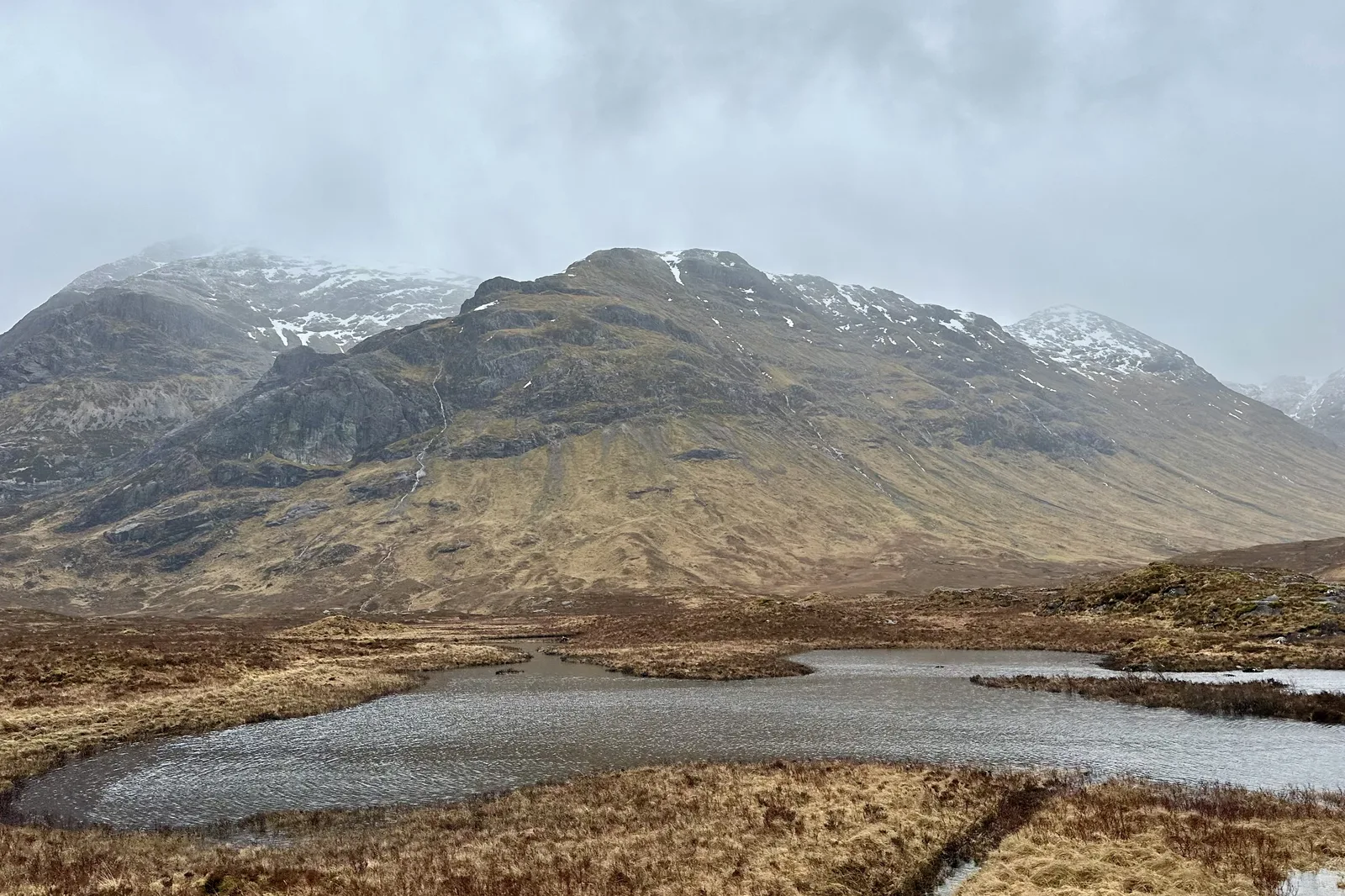 A snow streaked Highland peak above a lochan in Glencoe, Scotland