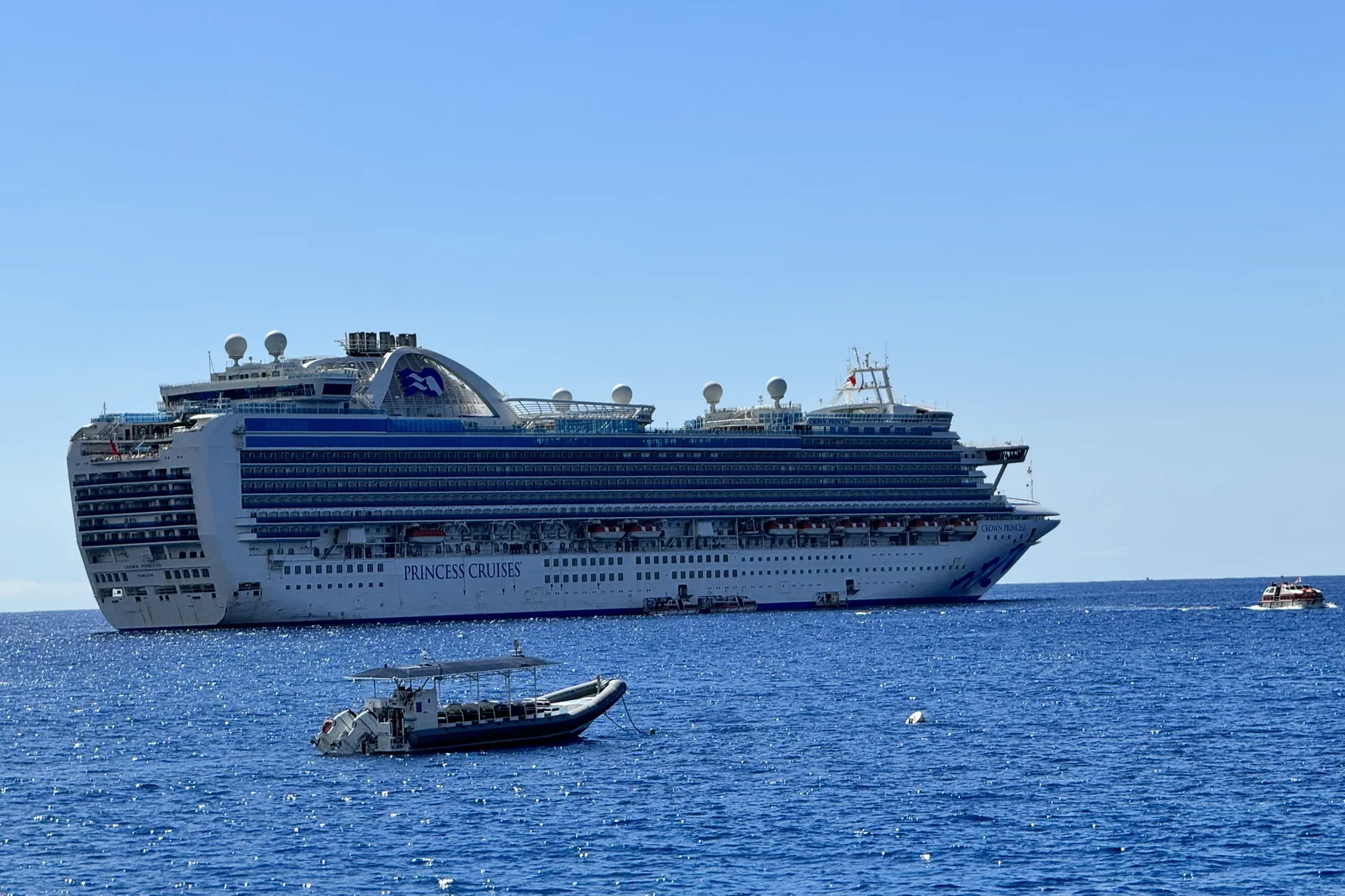 Crown Princess lying at anchor off Kailua-Kona with an orange ship's tender under way toward shore