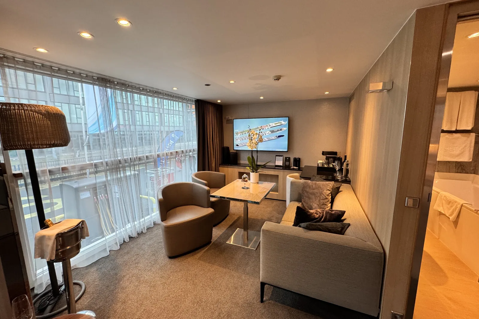 A cabin aboard Scenic Opal with a sofa, two armchairs around a low table, and a wall of glass looking out over the water