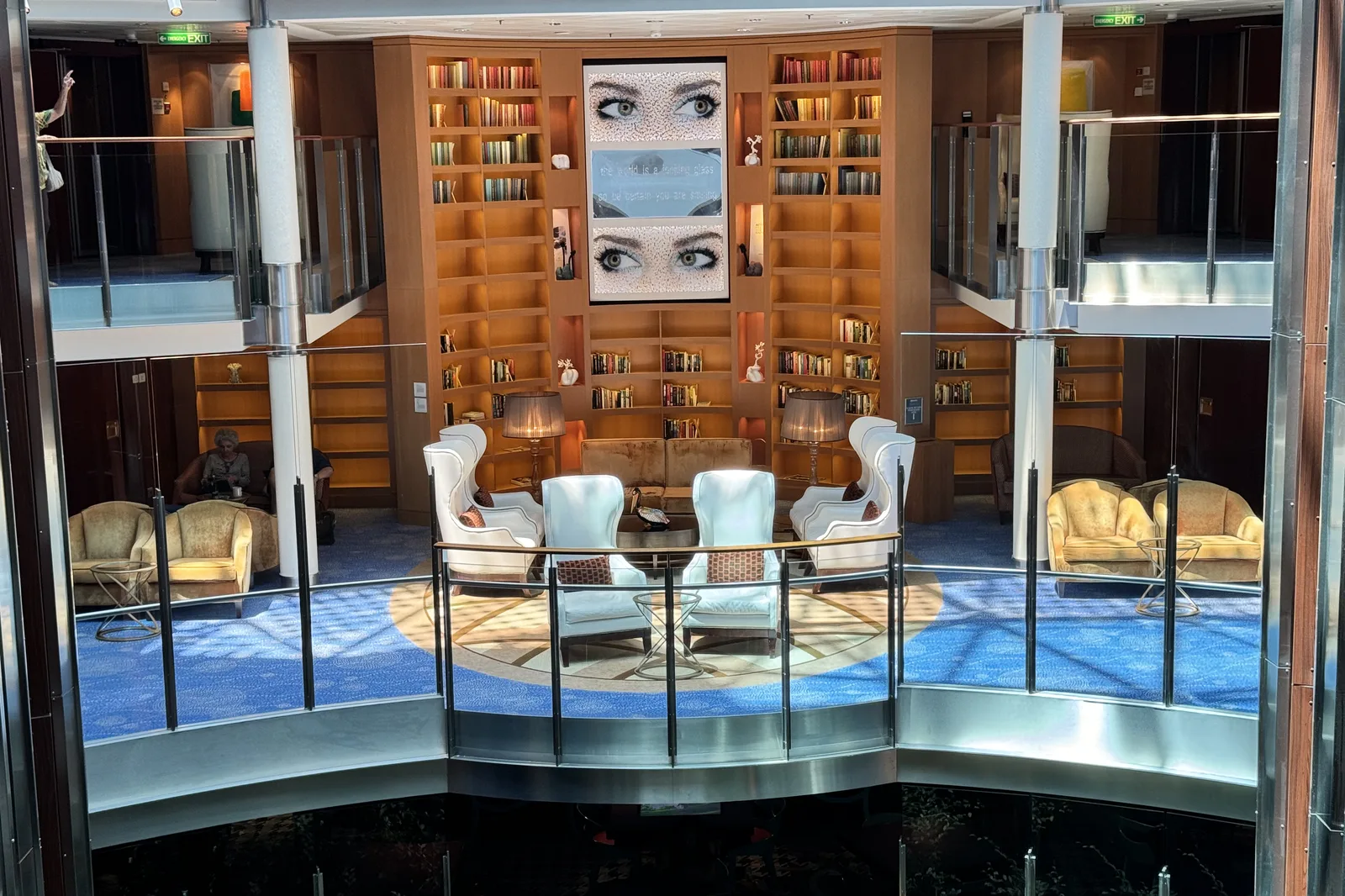 The two-deck library lounge on Celebrity Reflection, with white armchairs and floor to ceiling bookshelves