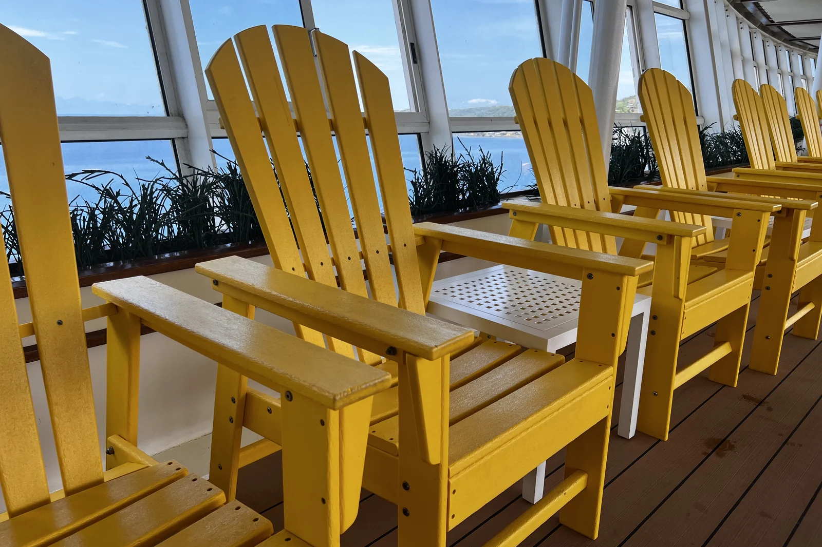 A row of yellow deck chairs aboard a Royal Caribbean ship looking out through tall windows to the blue Caribbean