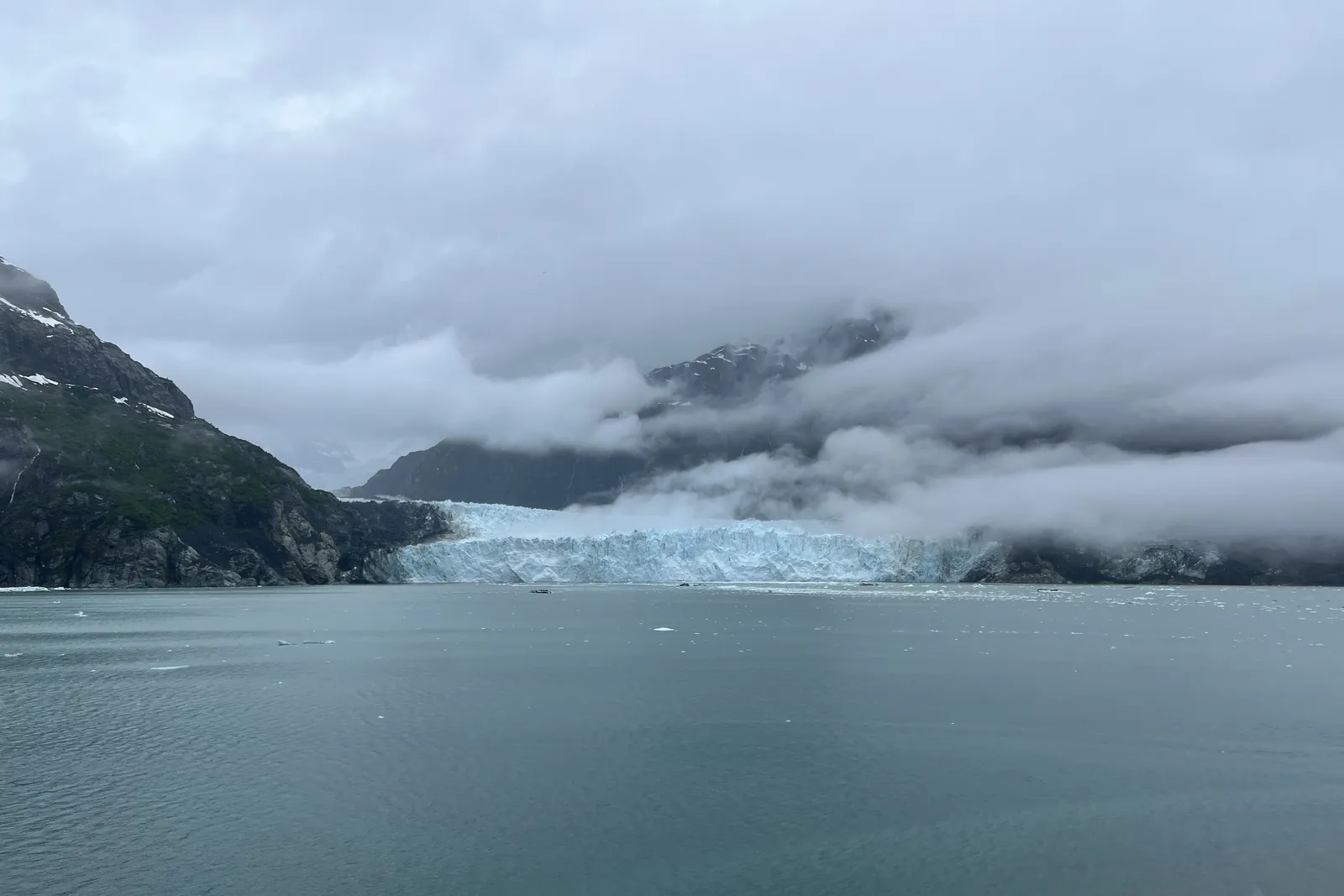 A tidewater glacier meeting the sea beneath low clouds in Glacier Bay, Alaska